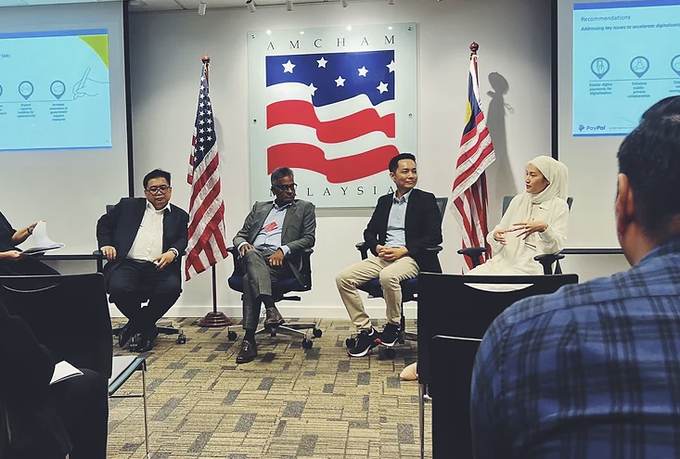 Panel discussion at AMCHAM Malaysia, four panellists seated in front of the American and Malaysian flags.